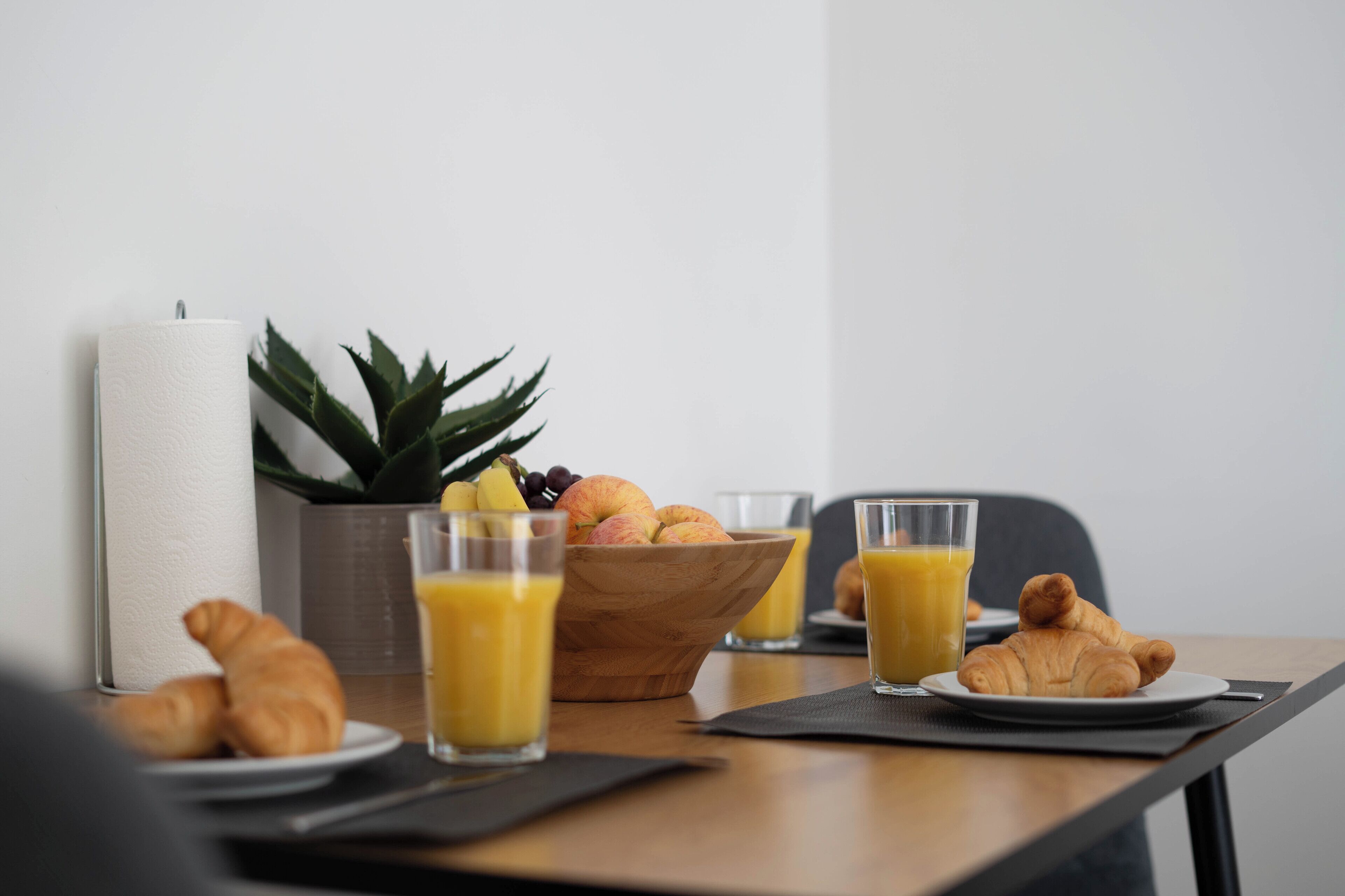 Een ontbijttafel met croissants, fruit en sinaasappelsap.