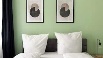 Ein Hotelzimmer mit einem Bett, zwei Kissen, einem Kopfteil, einem Nachttisch mit einer Lampe und zwei gerahmten abstrakten Kunstwerken an der Wand.