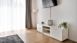 En moderne stue med et fladskærms-tv på væggen, et hvidt konsolbord med en plante og en gulvlampe.