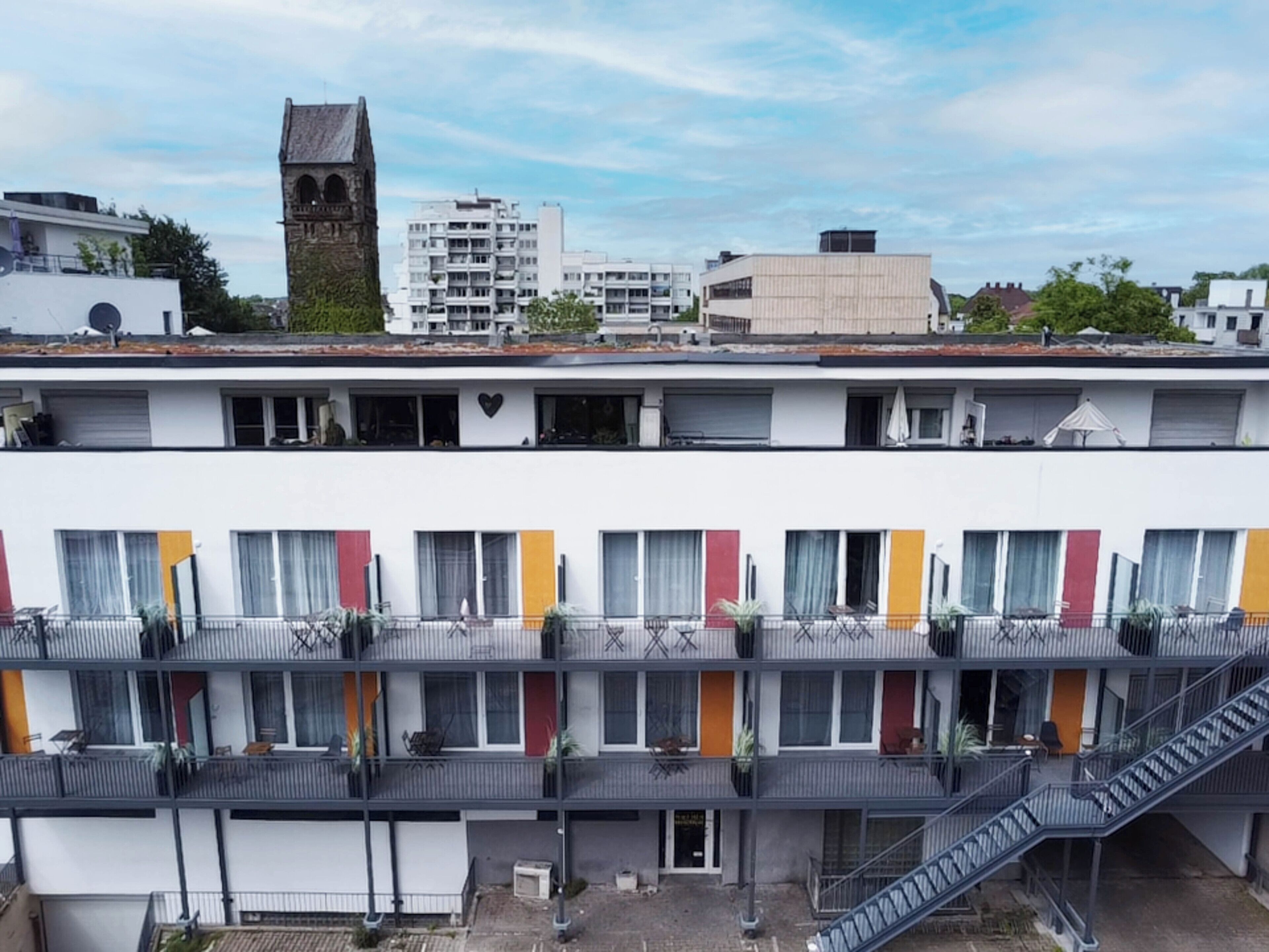 A multi-story hotel with balconies, a central staircase, and a view of surrounding buildings.