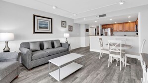 Un salon moderne avec un canapé gris, une table basse blanche et un coin repas comprenant des chaises blanches et une petite table.