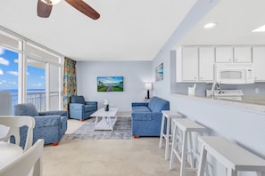Relax in this spacious living room with a large window offering a view of the outdoors, a flat-screen TV, and comfortable seating options.