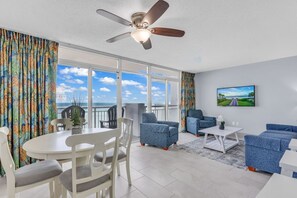 Enjoy ocean views from the large window in this spacious living room, featuring a dining table, sofas, and a mounted TV.