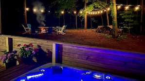 Ett bubbelbad med en träaltan, omgivet av träd och ljusslingor.