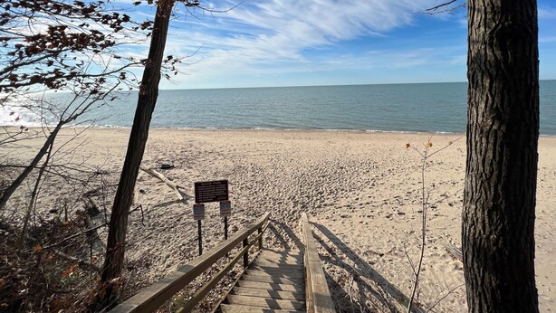 En träpromenad som leder till en strand, med en skylt som visar ”BAGAI PARK” och en utsikt över havet.