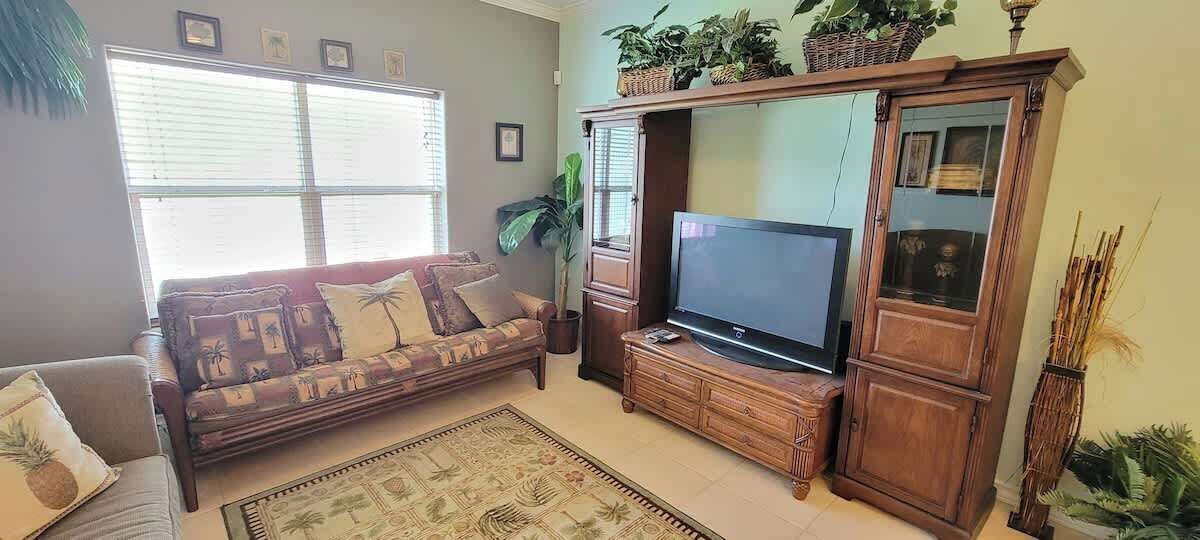 Ein Wohnzimmer mit einer Couch, Fernseher, einem Holzkabinett und einem großen Fenster mit Jalousien.
