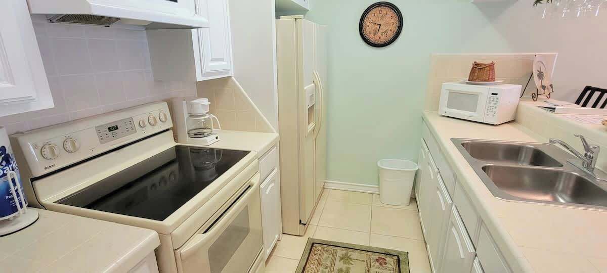 A compact kitchen with a stove, microwave, sink, and a clock on the wall.