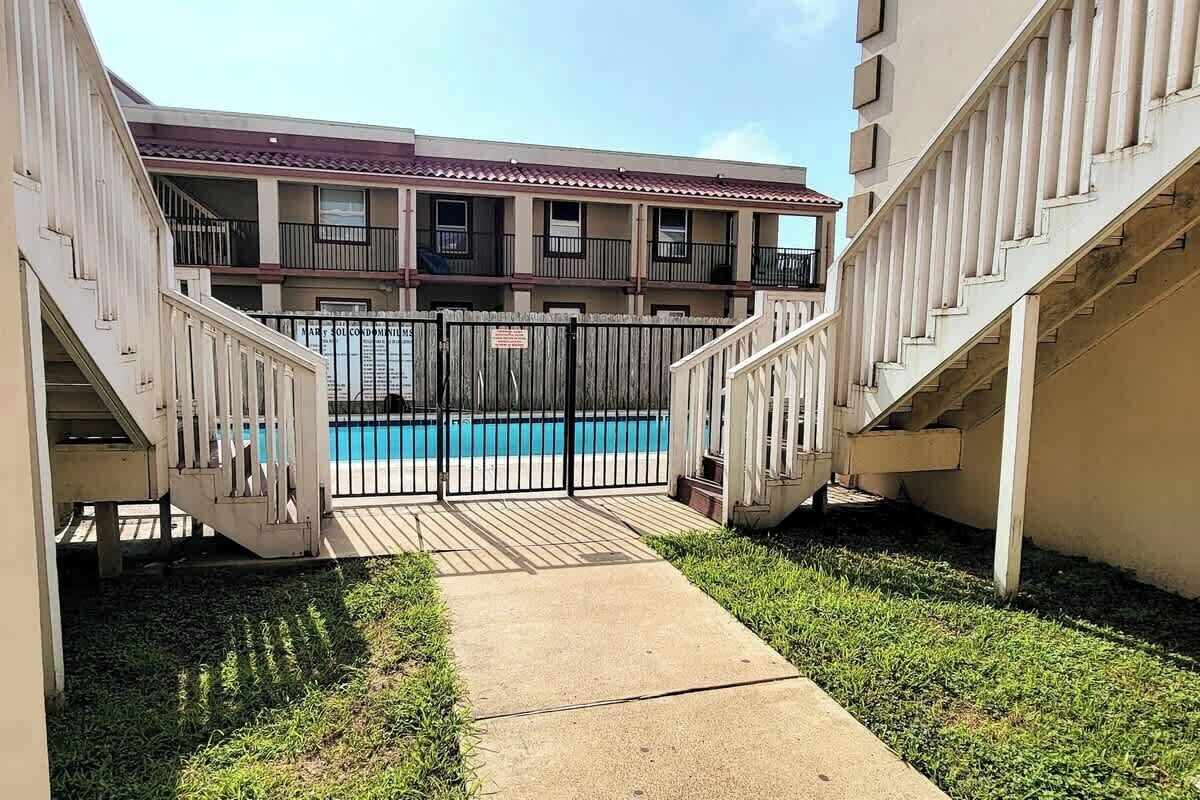 A pool area with a gated entrance, a concrete pathway, and a building with balconies.