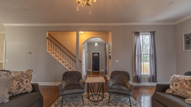 A spacious living room with a marble coffee table, two leather armchairs, a sofa, and a chandelier. A staircase leads to another room.