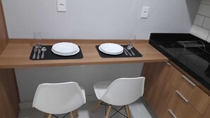 A compact kitchen with two white chairs, a wooden countertop, and a black stove. - Vista Bela (Tres Rios)