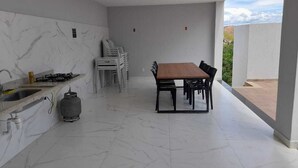 A modern kitchen with a gas stove, sink, and marble backsplash. There is a dining area with a table and chairs. - Vista Bela (Tres Rios)