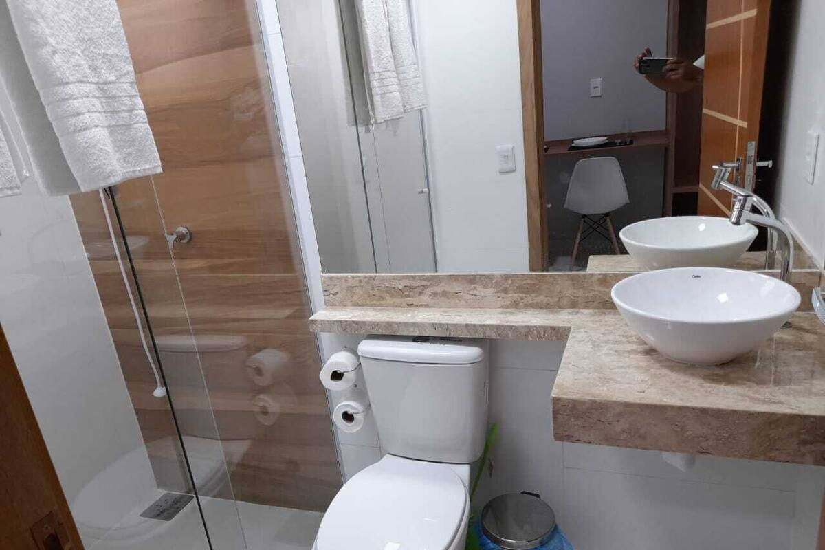 Un baño moderno con ducha envuelta en vidrio, inodoro blanco y lavamanos con encimera color beige.