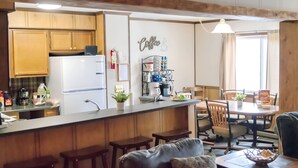 Eine Küche mit Holzausstattung, einem Kühlschrank, einer Kaffeestation und einem Essbereich mit Tisch und Stühlen.