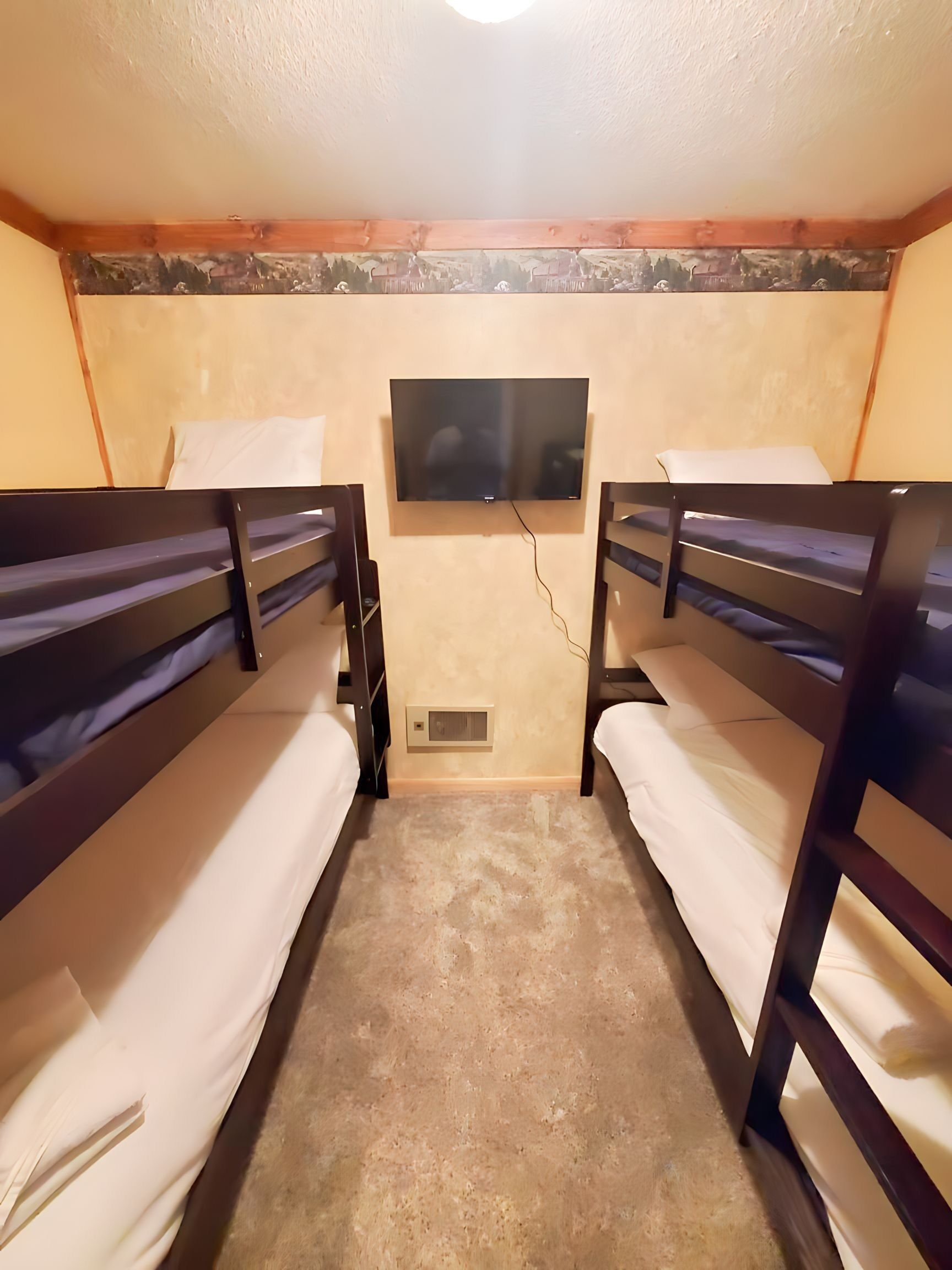 A room with two bunk beds, a television mounted on the wall, and a small vent on the floor.