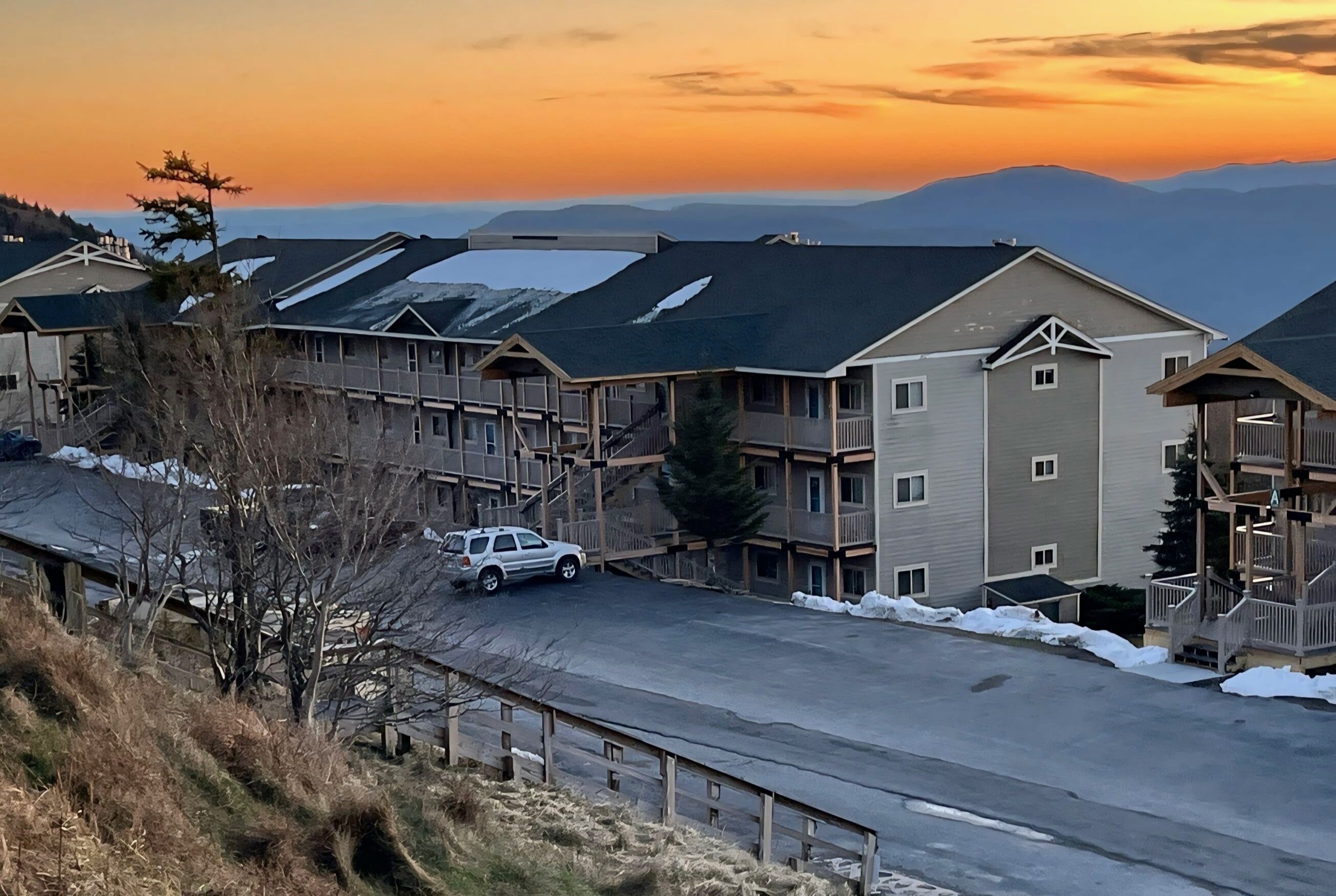 Zona residencial con edificios de varios pisos, estacionamiento y vista a montañas distantes al atardecer.