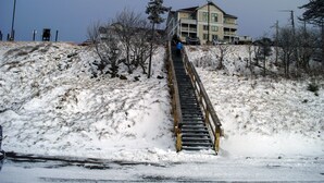 Ein verschneiter Hang mit einer Holztreppe, die zu einem Gebäude führt.