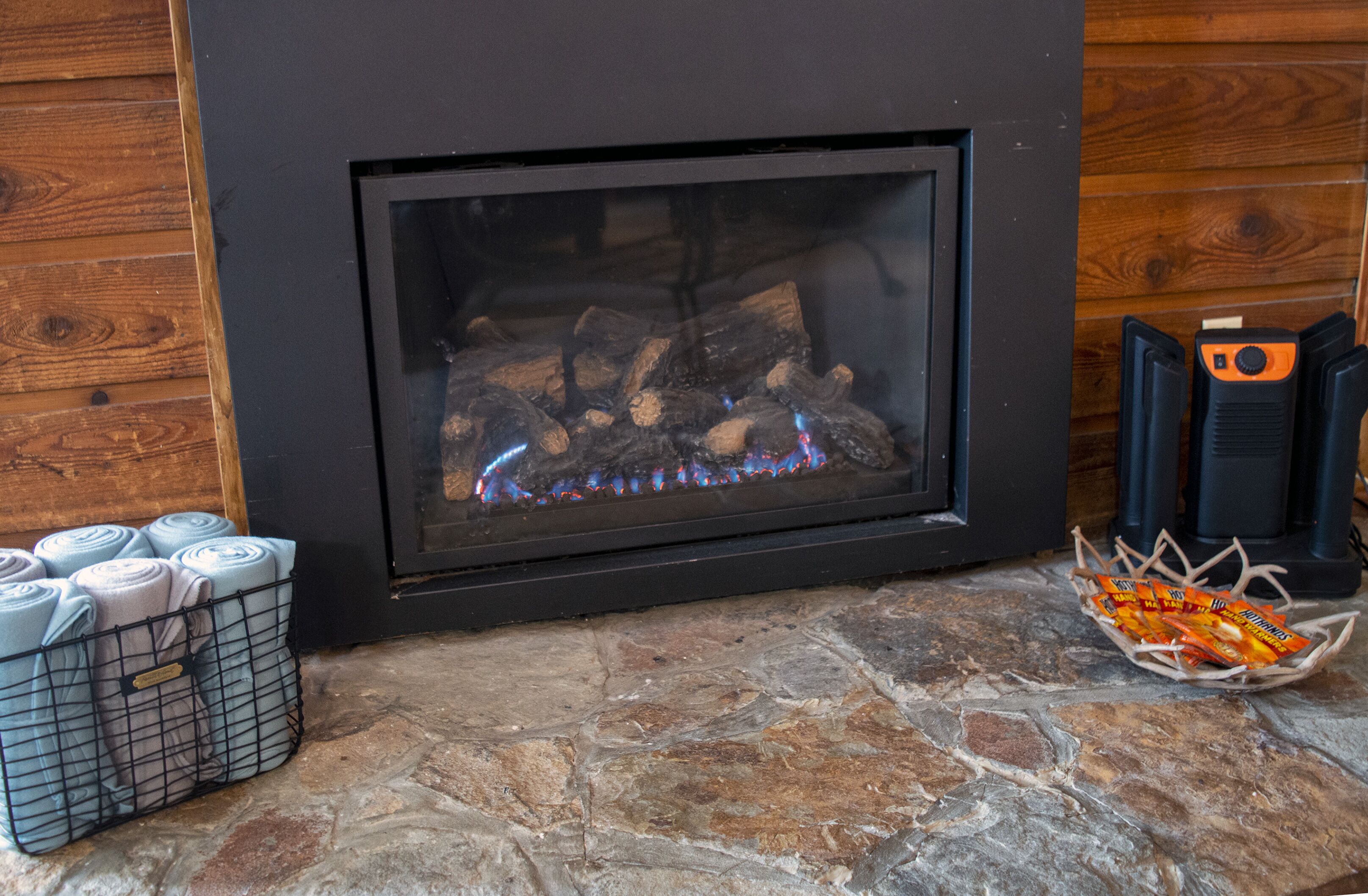 A fireplace with logs burning, a stone floor, and a basket of snacks.