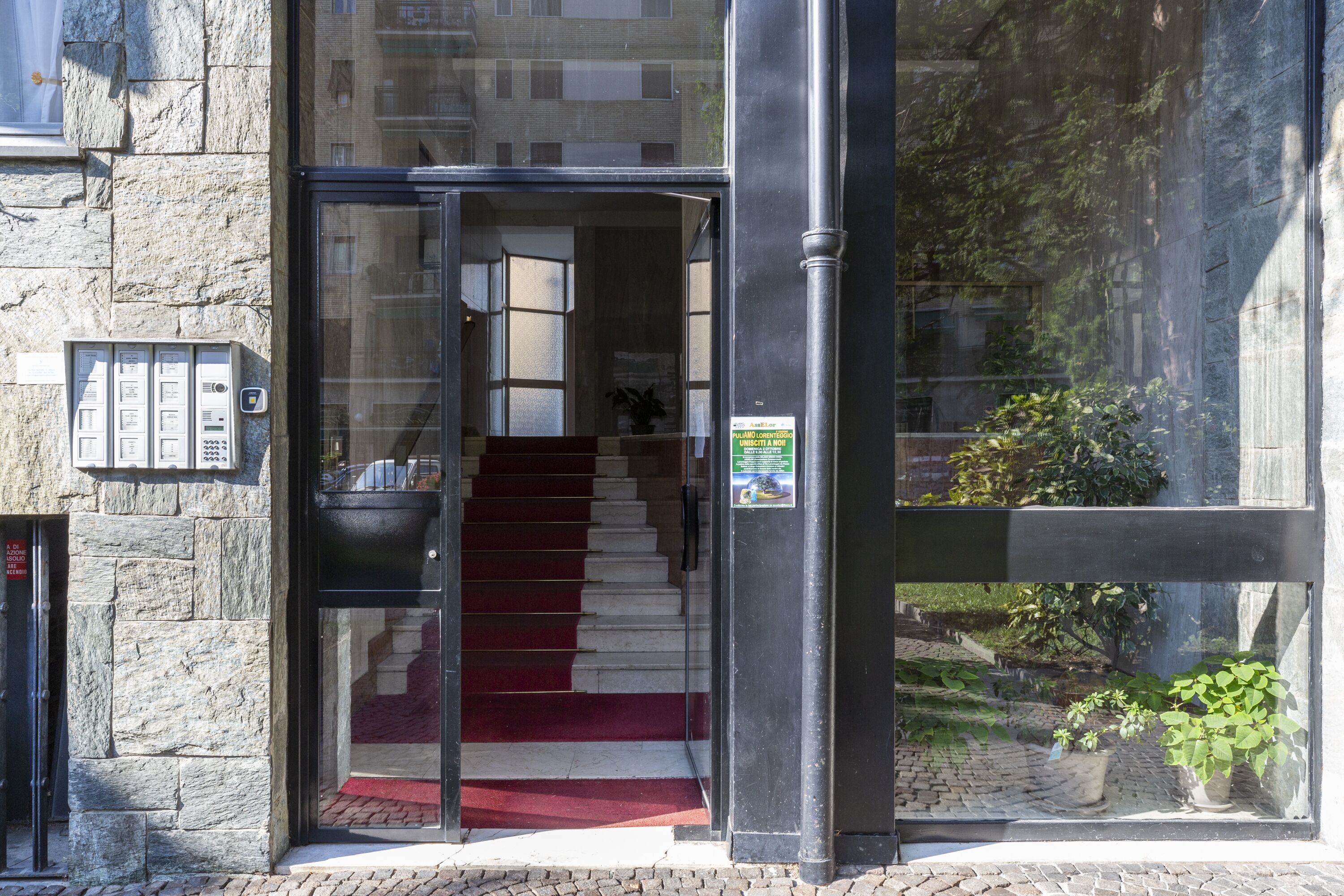 A building entrance with a glass door, a red carpet, and a stone wall.