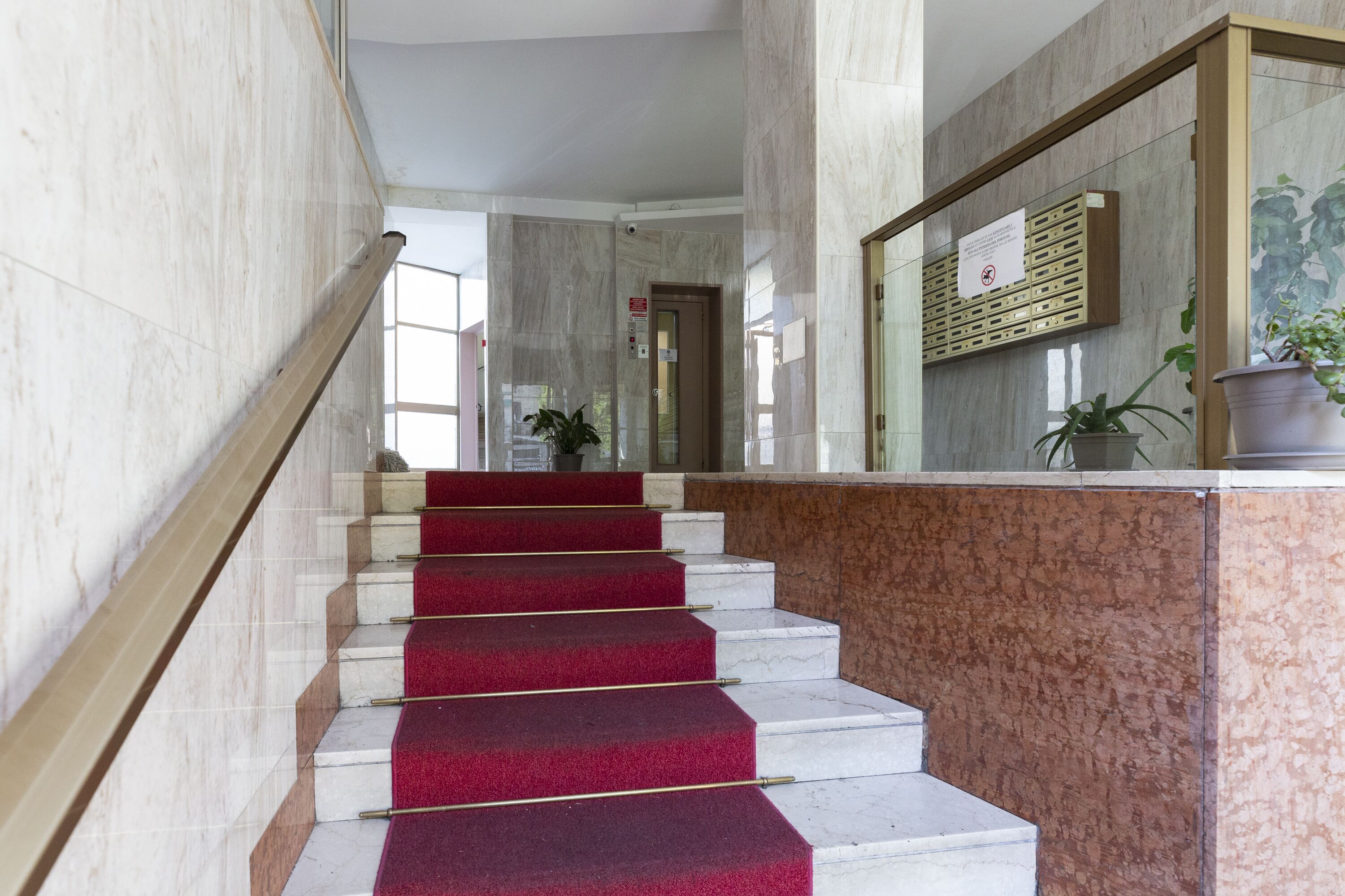 Un escalier en marbre, dont les marches sont recouvertes d’une moquette rouge, mène à un espace d’accueil.