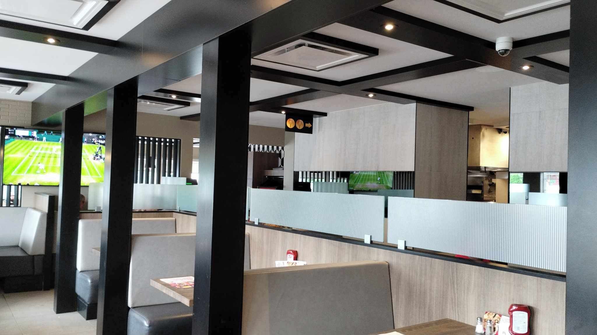 A modern restaurant with high tables and booths, a sports screen, and a menu board.