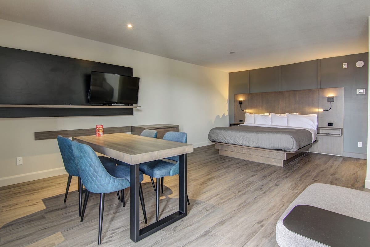 Une chambre d’hôtel moderne équipée d’un lit, d’un téléviseur fixé au mur, d’une table à manger avec des chaises et d’un petit coin salon.