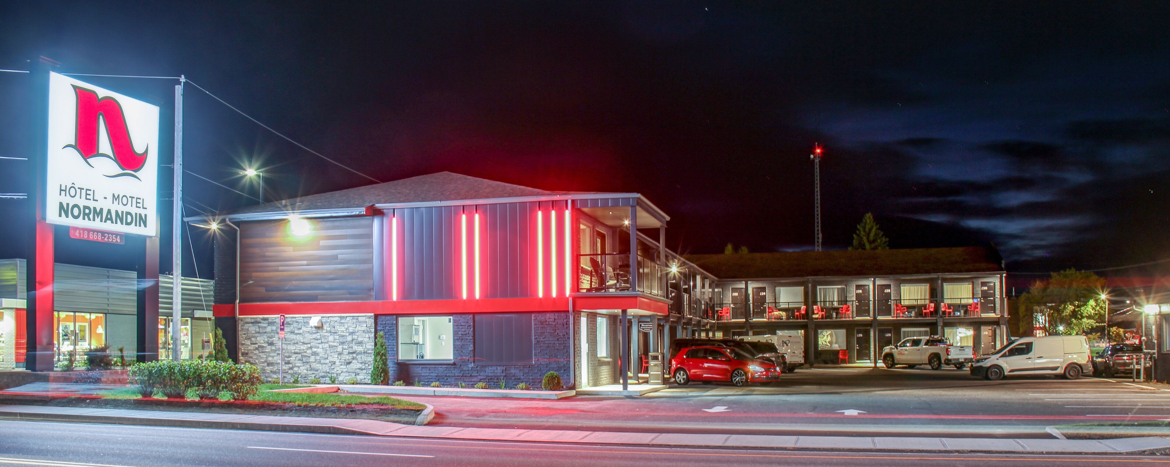 A modern hotel with a prominent sign, multiple parking spaces, and a well-lit entrance.