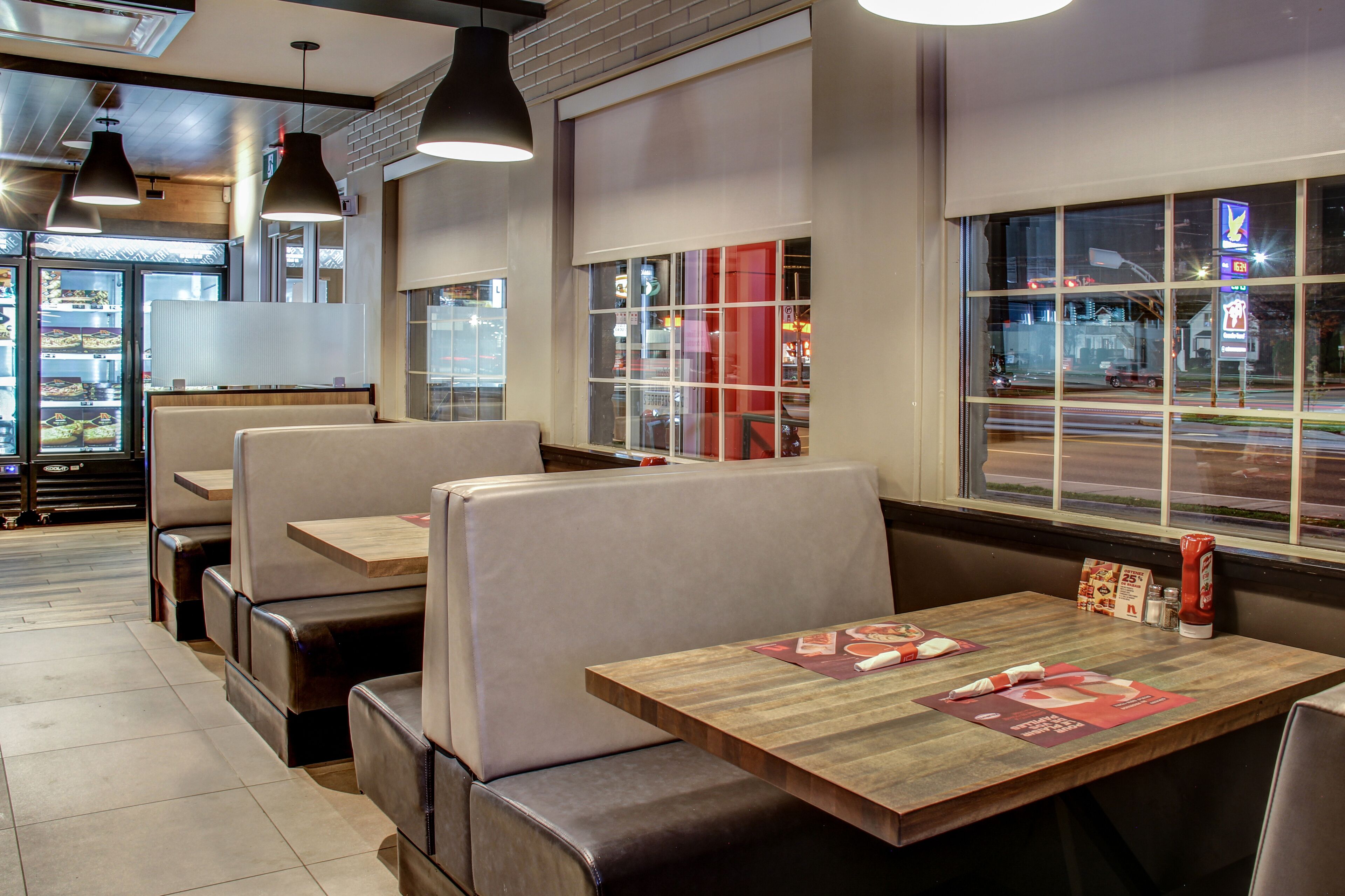 A restaurant interior with booths and tables, a brick wall, and a view of the street through large windows.