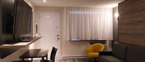 A modern living room with a flat-screen TV, a dining table with chairs, a sofa, and a yellow armchair.