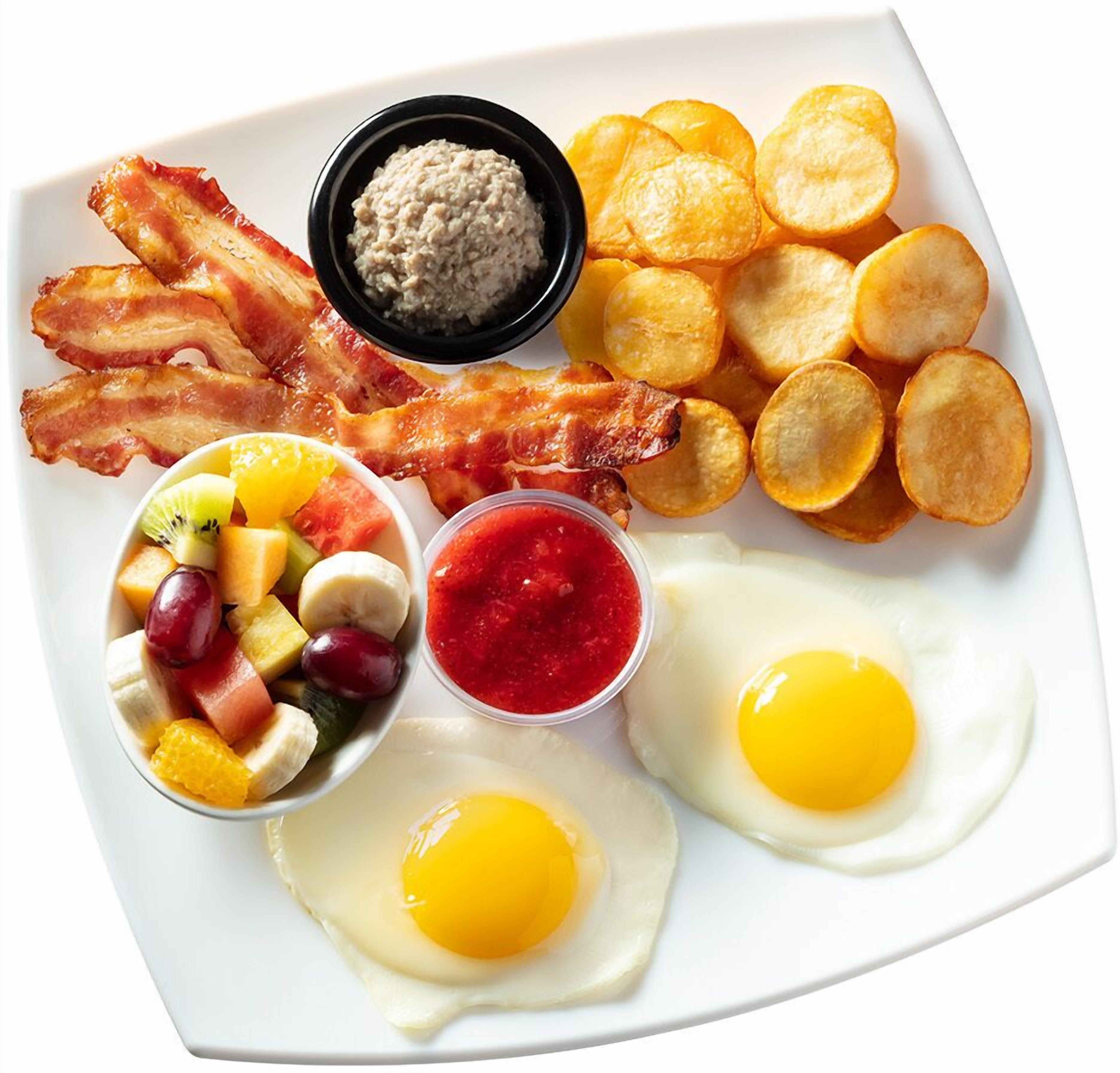 Un plato de desayuno con tocino, huevos, patatas ralladas, fruta y salsas.