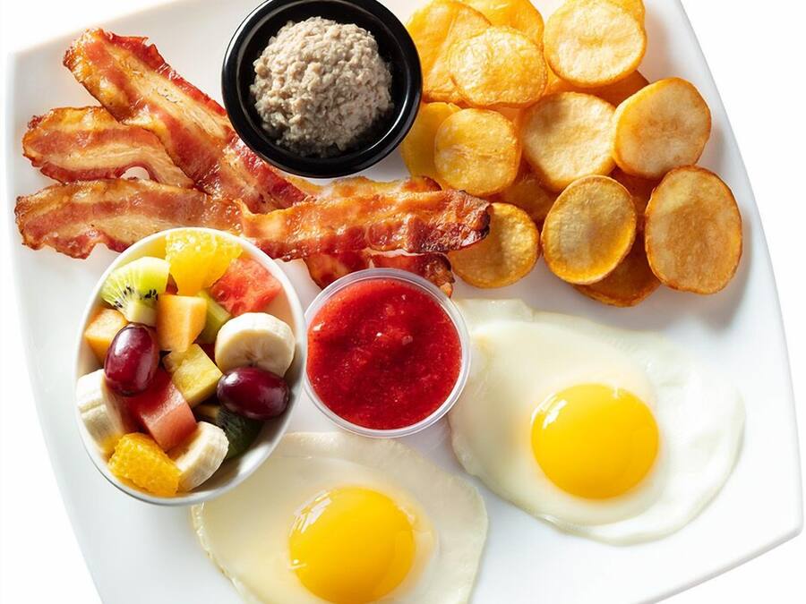 A breakfast plate with bacon, eggs, hash browns, fruit, and condiments.