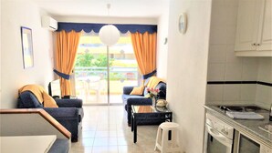 A compact living space with a kitchen area, a dining table, two sofas, and a small table with a vase and a telephone. - 2 Bed Hotel Apt. Sleeps 3/4, Five minutes walk to Beach, Shops & Restaurants  (Costa Adeje)