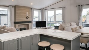 Een moderne keuken met een marmeren aanrecht, grijze kasten en een ingebouwde televisie. Twee hanglampen, een open haard en een groot raam met uitzicht.