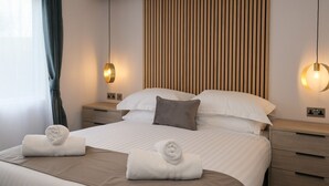 Een moderne hotelkamer met een groot bed, twee nachtkastjes, een houten spijbelborden hoofdeinde en twee hanglampen.