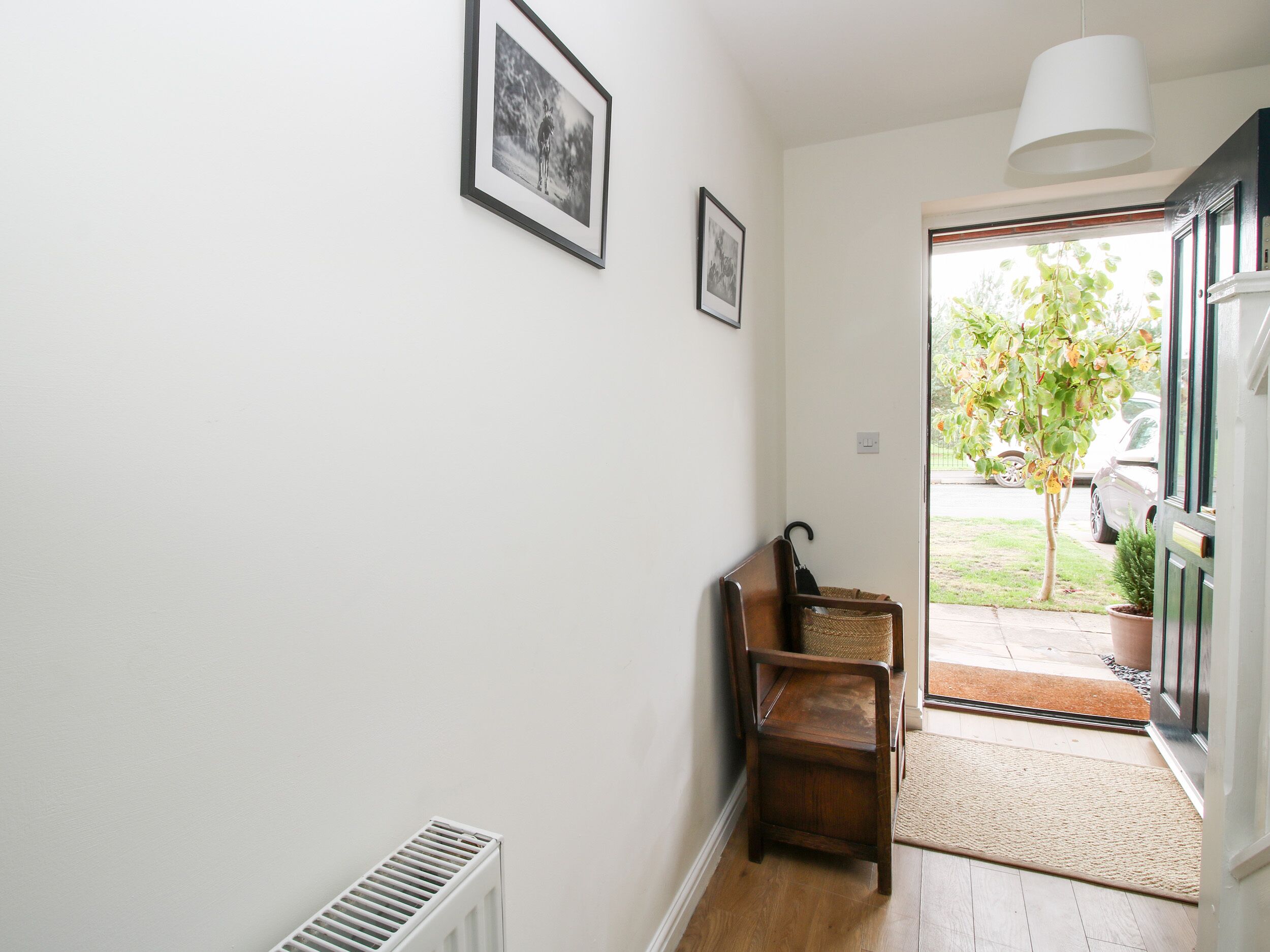 A hallway with a radiator, a chair, a door leading outside, and two framed pictures on the wall.
