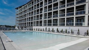 Un hotel moderno con un amplio espacio de piscina, varios balcones y un cielo despejado.