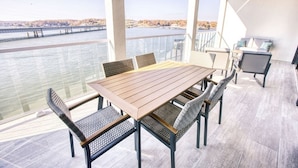 Una terraza con mesa y sillas de madera, con vistas a un cuerpo de agua y un puente.
