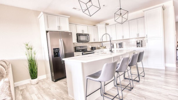 Una cocina moderna con armarios blancos, un refrigerador de acero inoxidable, un microondas y una isla central con taburetes de bar.