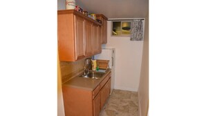 A small kitchen with wooden cabinets, a sink, and a window with a curtain. - Slopeside. Buy your ski/snowboard tickets on line! (Big Bear Lake)