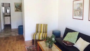 A living room with a striped armchair, a black sofa, and a coffee table with a plant. There is a ceiling fan, a kitchen in the background, and a painting on the wall. - Slopeside. Buy your ski/snowboard tickets on line! (Big Bear Lake)