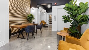 A modern interior with a wooden slat wall, a dining area with a wooden table and chairs, and a large green plant. - Le Sand & Stone Hôtel (Montreal)
