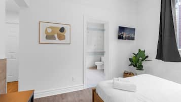 Quarto com cama, mesa de cabeceira, planta em vaso e um quadro na parede.