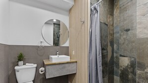 A modern bathroom with a toilet, sink, mirror, and shower. - Le Sand & Stone Hôtel (Montreal)