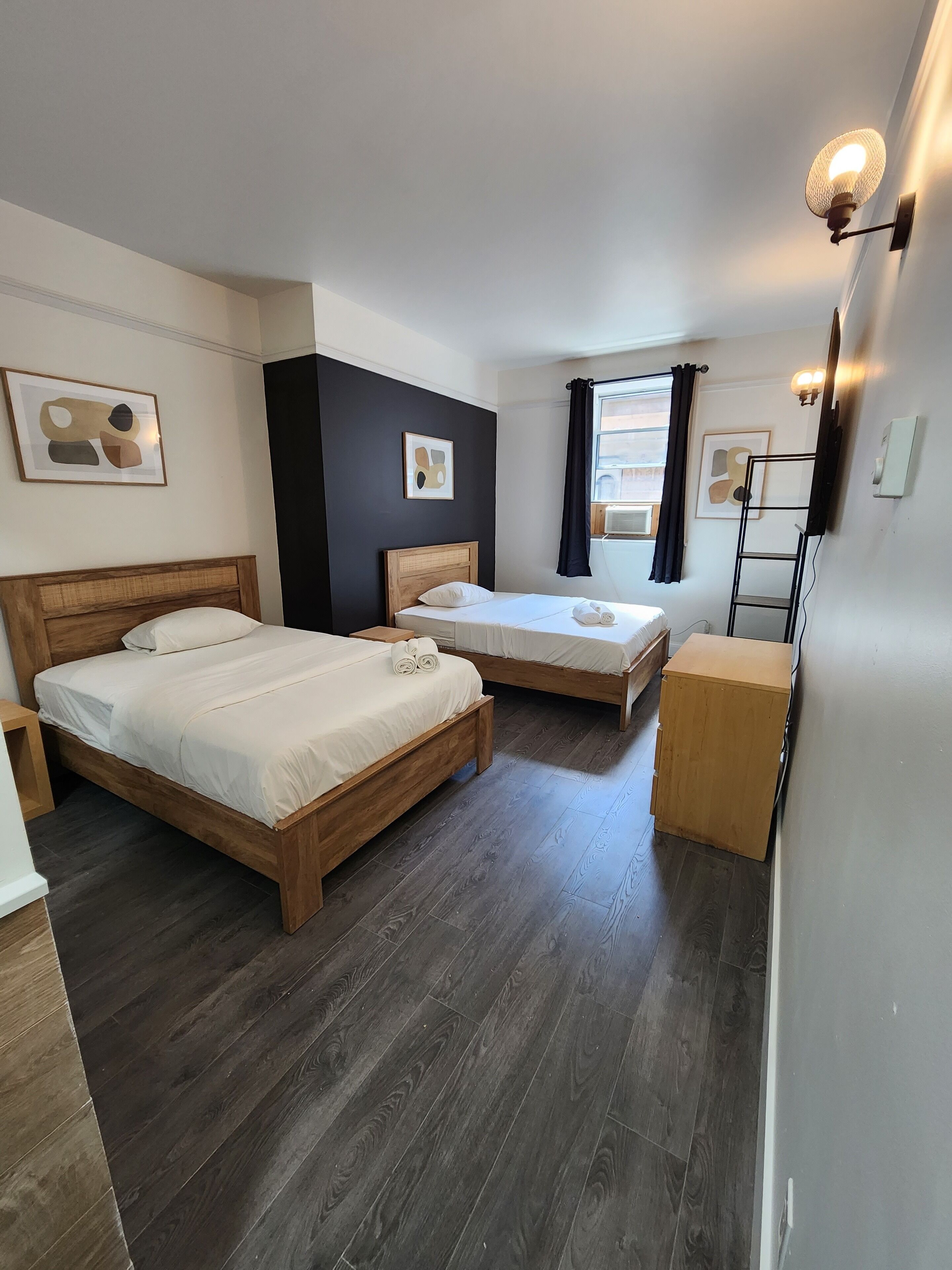 Ein Hotelzimmer mit zwei Holzbett, einer kleinen Holzkiste und einem Fenster mit Vorhängen.