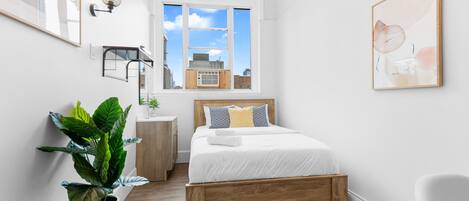 Un dormitorio moderno con una cama de madera, paredes blancas, un ventanal grande y una planta en maceta.