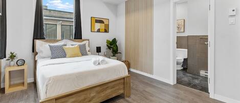 A modern bedroom with a wooden bed, a bedside table with a clock, a potted plant, and a window with curtains.