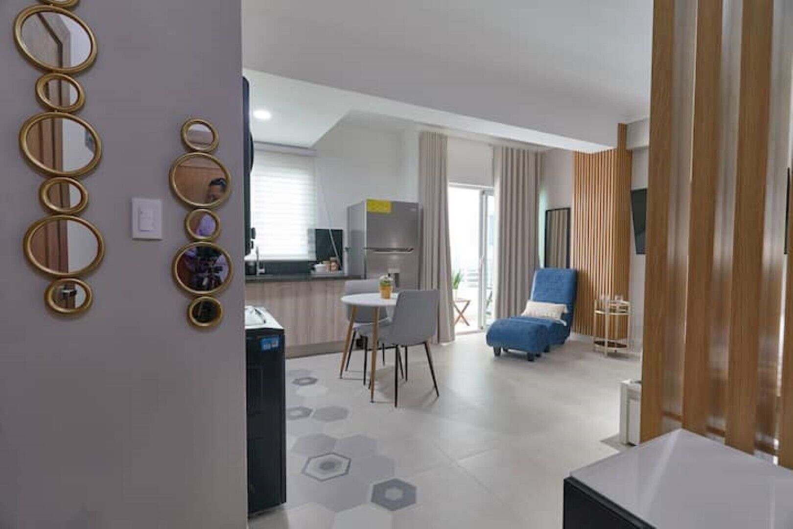 Een moderne woonkamer met een blauwe fauteuil, een eethoek met een kleine tafel, en een keuken op de achtergrond.