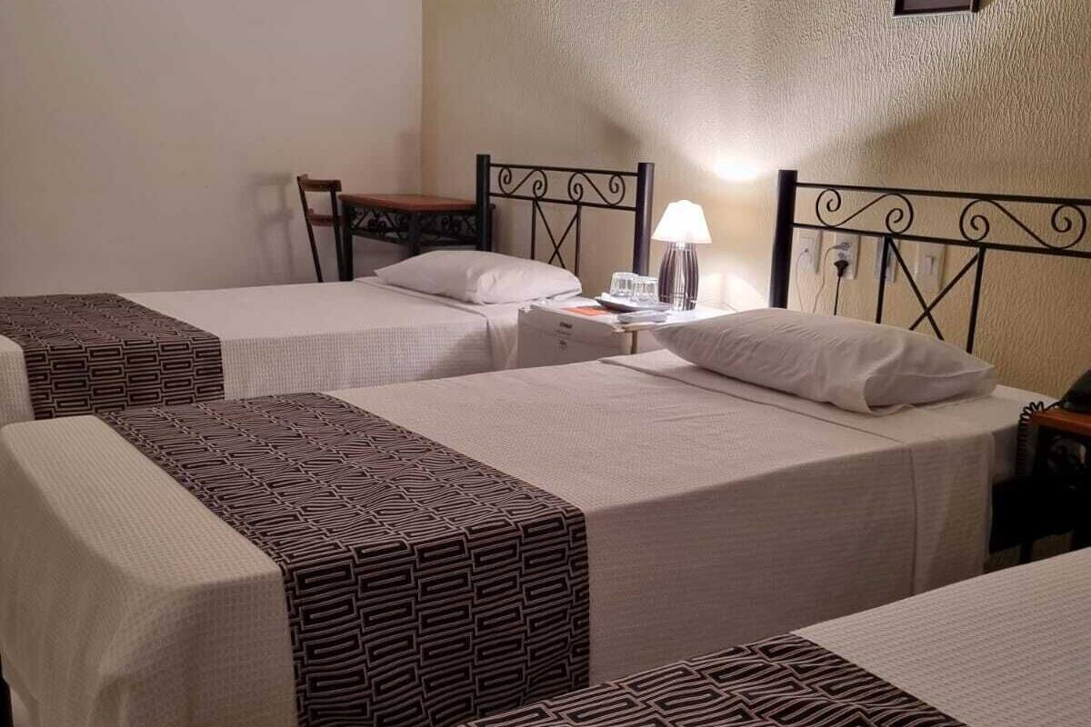 Habitación de hotel con dos camas, cada una con una colcha estampada, una mesita de noche con lámpara y un cuadro en la pared.