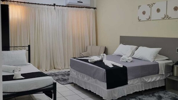 Une chambre d’hôtel avec deux lits, une grande fenêtre avec des rideaux, un appareil de climatisation et un tapis moelleux.