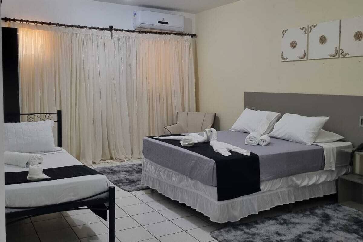 Una habitación de hotel con dos camas, un ventanal con cortinas, un equipo de aire acondicionado y una alfombra mullida.