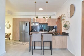 Une cuisine moderne dotée d’un îlot central, d’appareils électroménagers en acier inoxydable, de luminaires suspendus et d’un décor minimaliste.